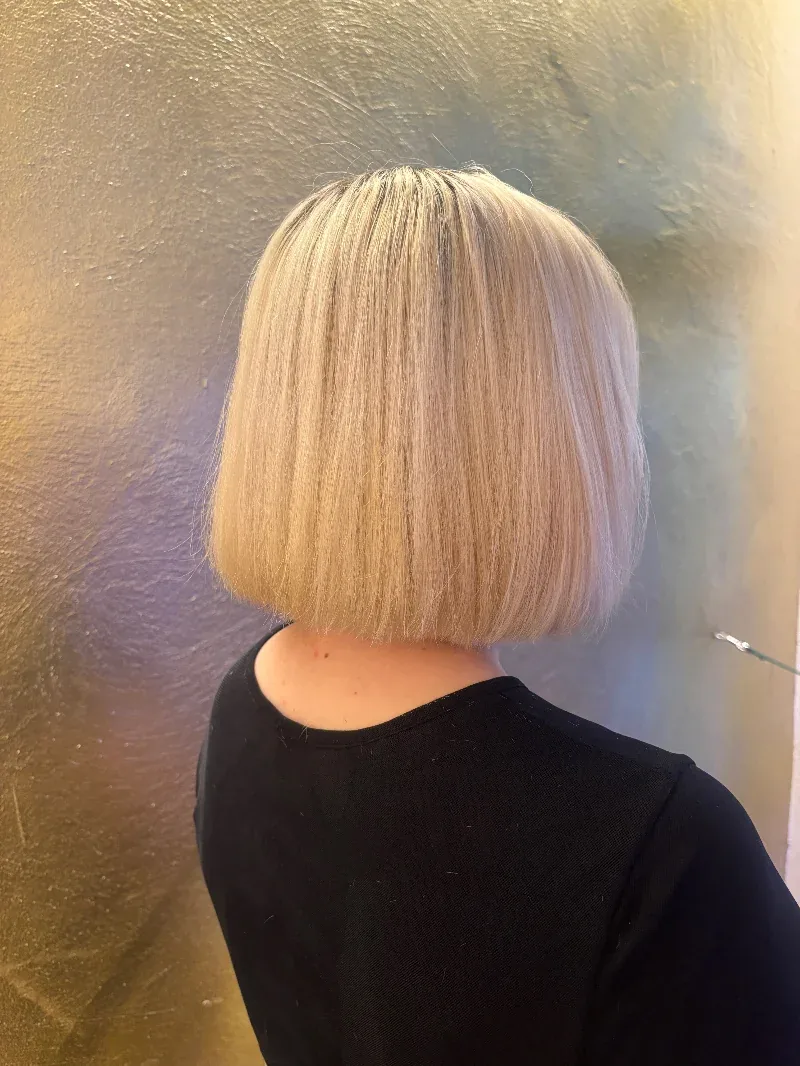 Platinblonder, stumpfer Bob von hinten vor einer goldenen Wand