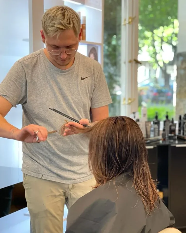 Maxim Elfmann prüft mit Kamm und Schere eine Haarsträhne am Stuhl